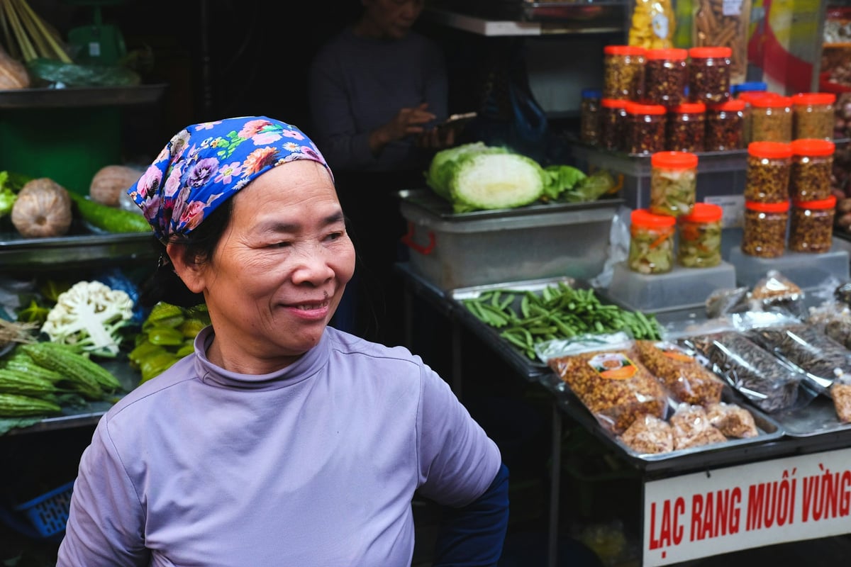 A street vendor smiling beside her stall of prepared food and jars