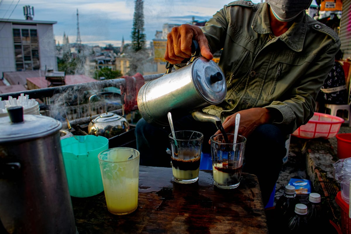 A street vendor pouring iced coffee into glasses at a pavement stall