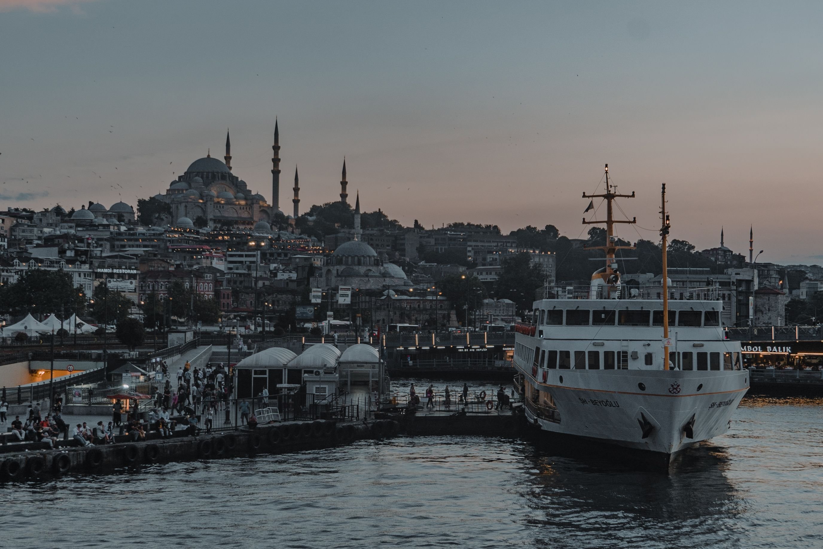 A Bosphorus ferry on the water with the city skyline and a mosque silhouette behind