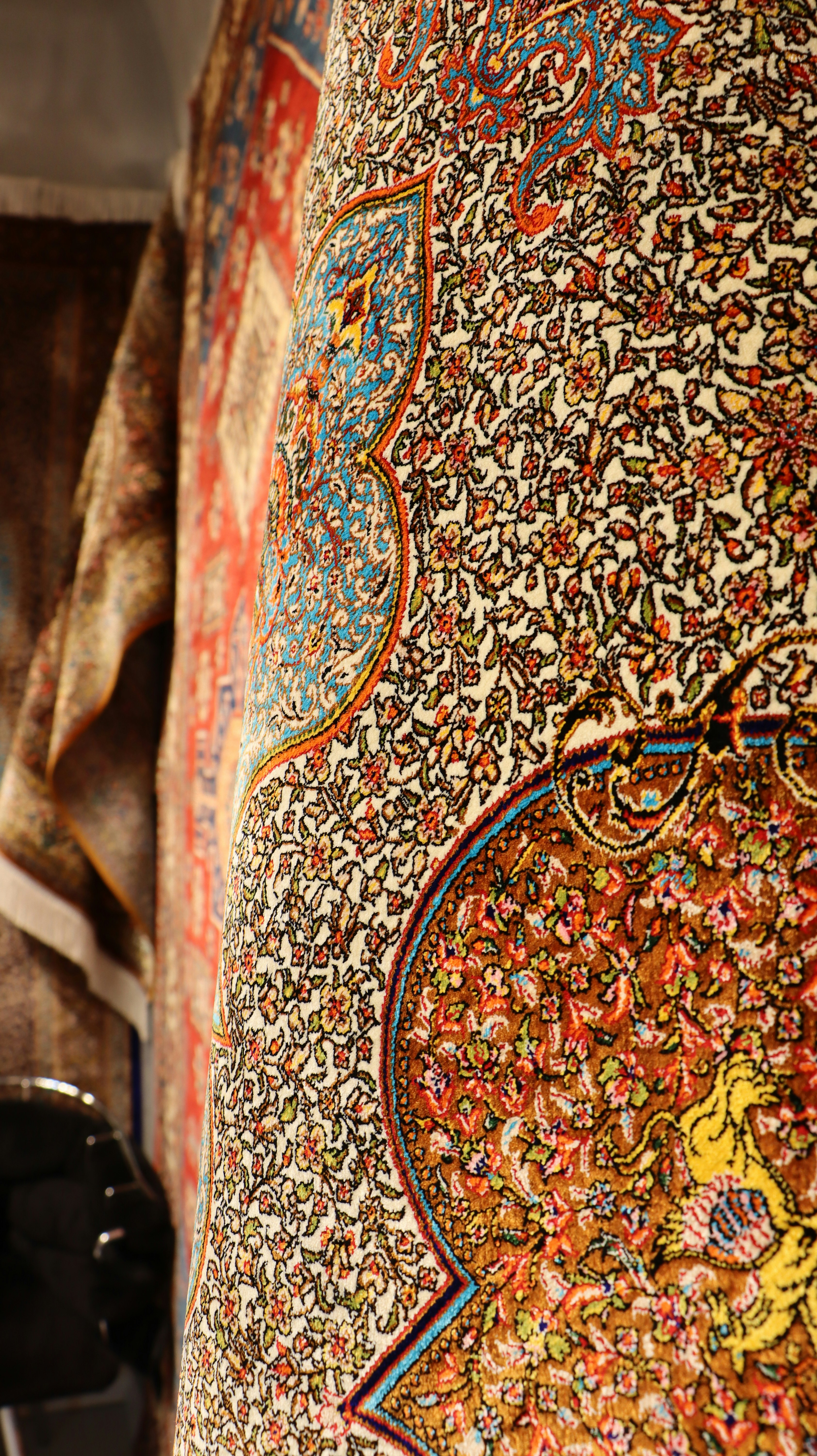 A carpet shop interior with stacks and hanging hand-knotted Turkish rugs in rich colors, no recognizable faces