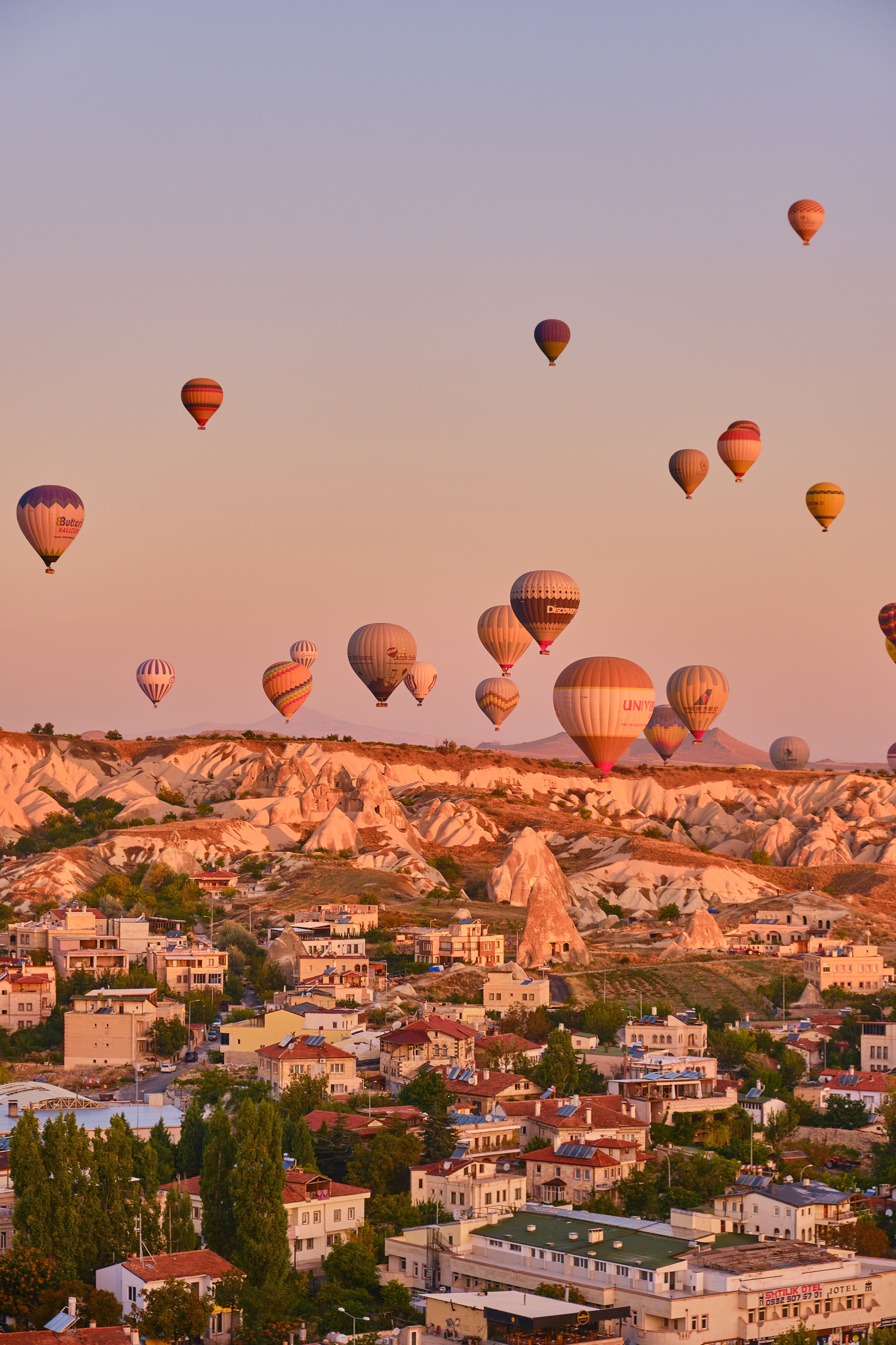 Dozens of colorful hot air balloons over the Cappadocia valley at sunrise with fairy chimneys below