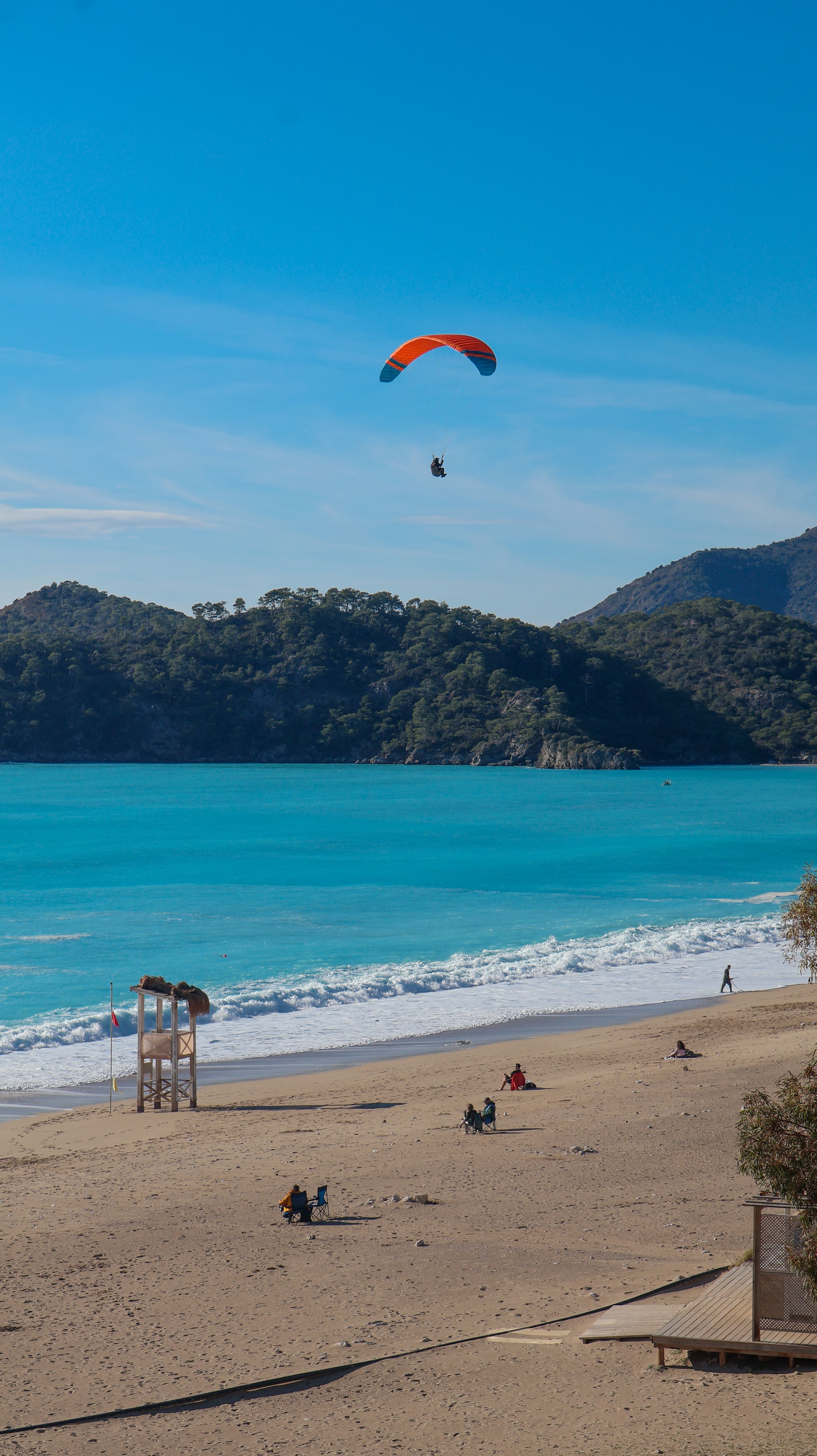 A tandem paraglider descending toward Ölüdeniz beach with the lagoon below