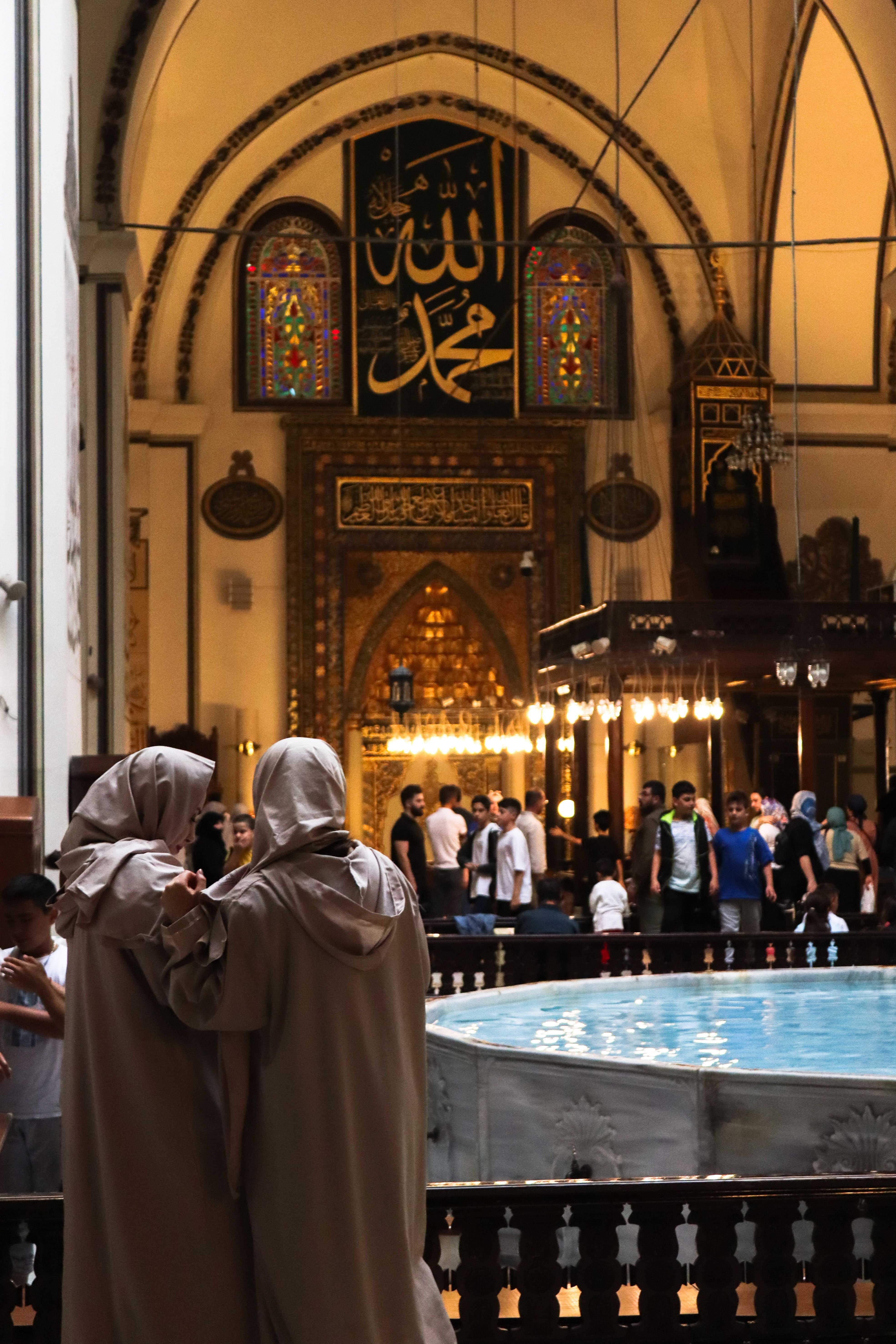 The interior of a grand Turkish mosque showing visitors dressed respectfully, no recognizable faces