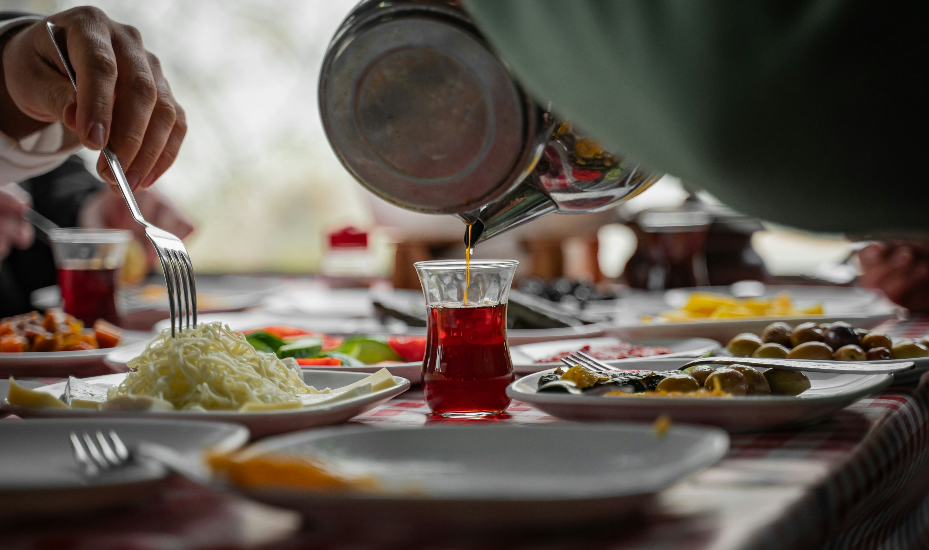 A lavish Turkish breakfast spread on a table — cheeses, olives, tomatoes, eggs, jams, bread, and tea, no recognizable faces